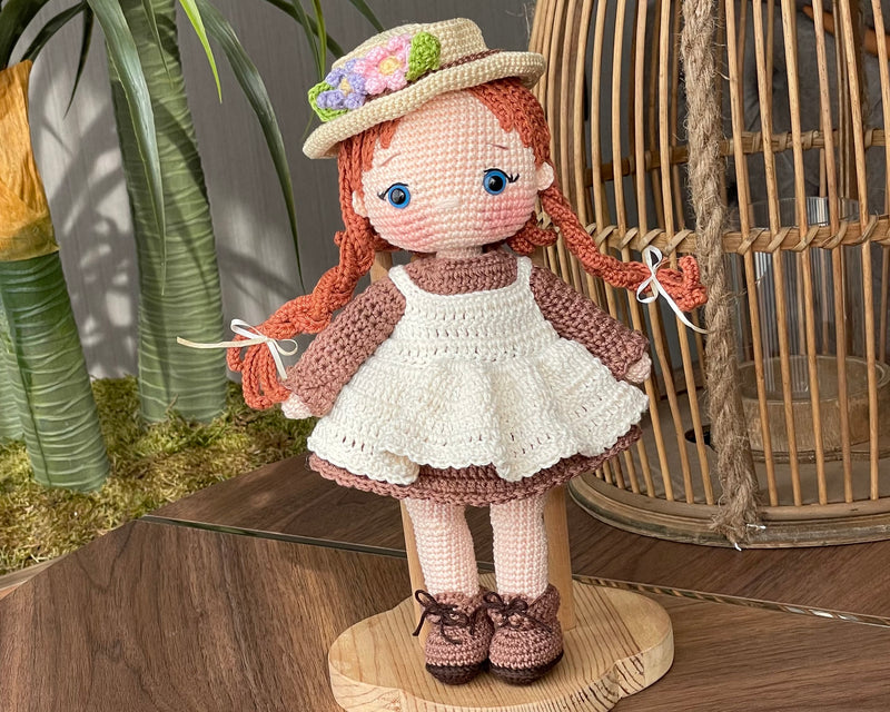 Handmade crocheted Anne Shirley Doll with long braided hair, wearing a white apron and a floral hat. The doll is customizable with a name on a leather label, perfect as a personalized gift or room decor.