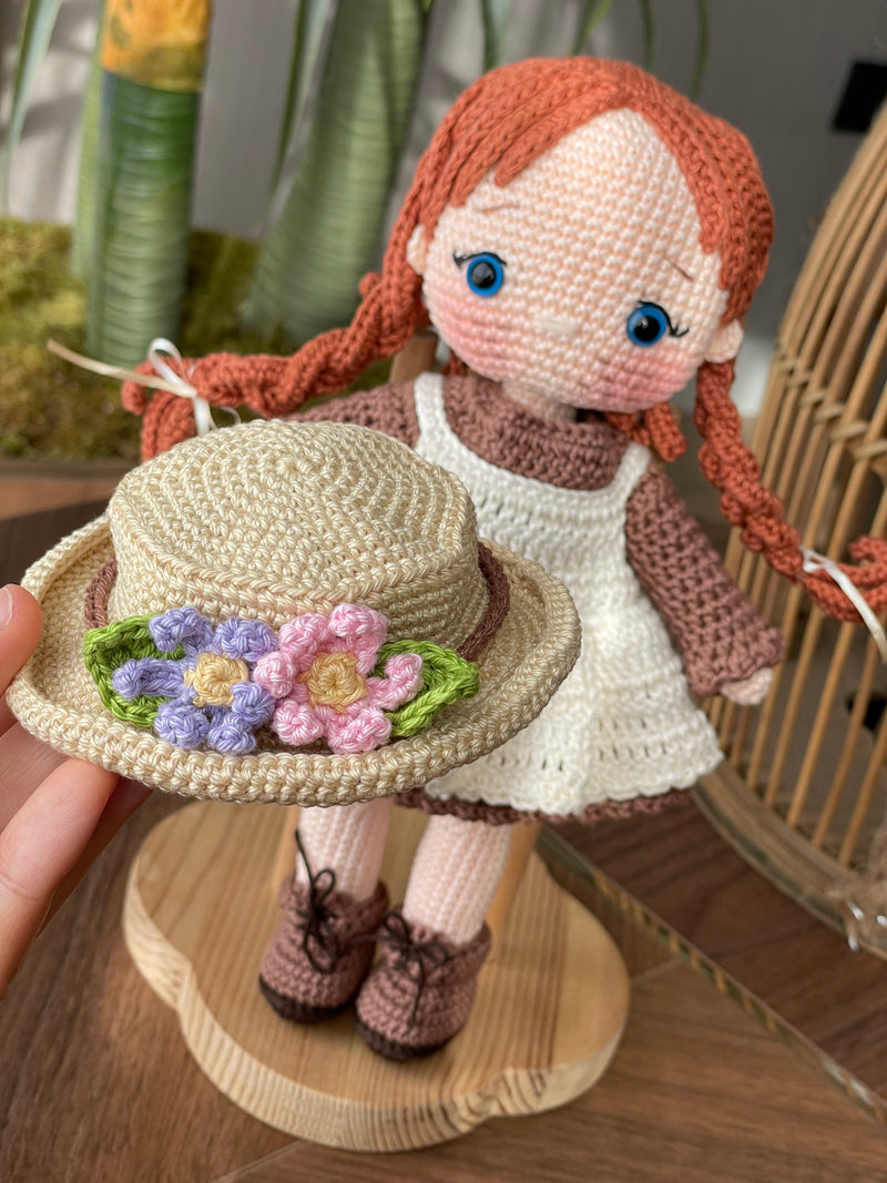 Handmade crocheted Anne Shirley Doll with long braided hair, wearing a white apron and a floral hat. The doll is customizable with a name on a leather label, perfect as a personalized gift or room decor.