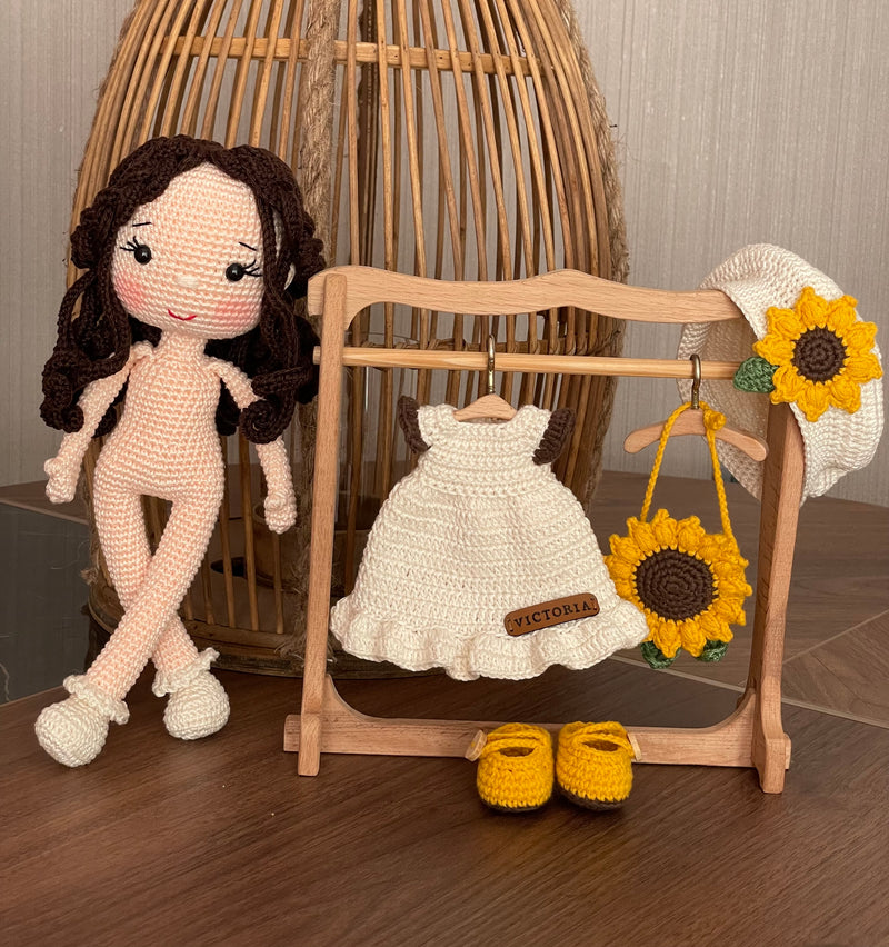 A handmade Sunflower Girl Doll with dark brown hair, wearing a white dress adorned with sunflowers, a matching sunflower beret, and yellow shoes, crocheted using the amigurumi technique and personalized with a custom name on a leather label.