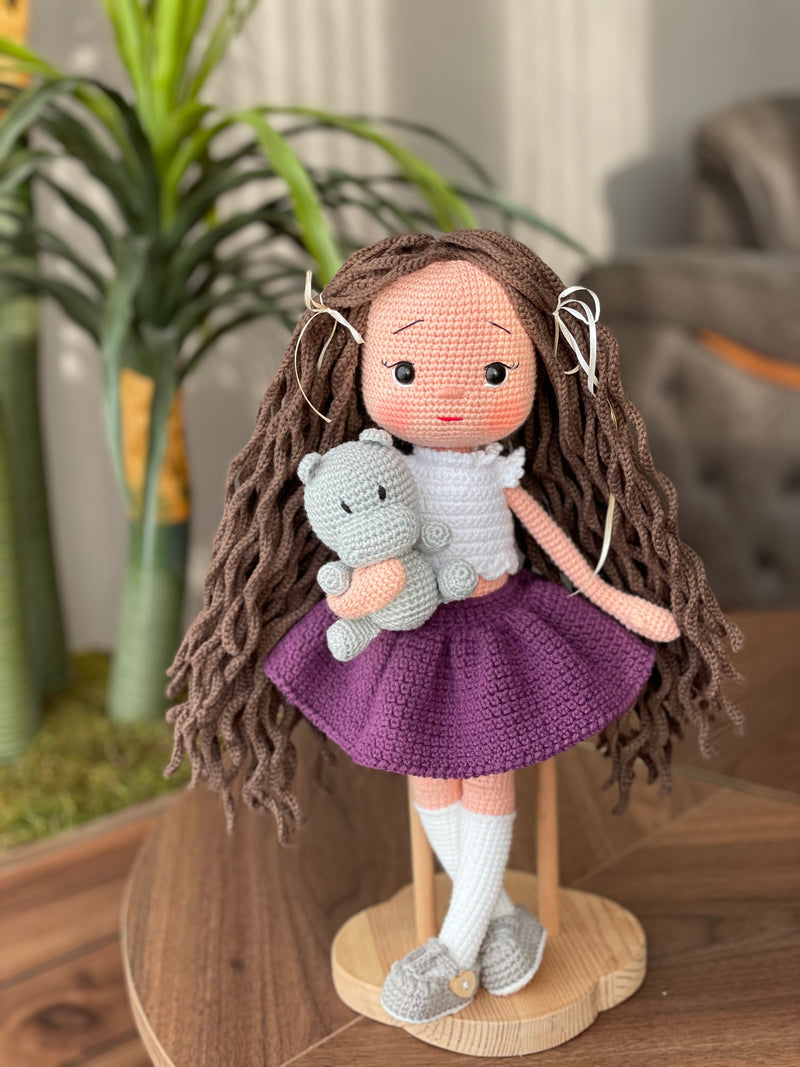 Handmade crocheted Purple Skirted Olivia Doll with long brown hair, a cute skirt, and a tiny hippo, customizable with a name on a leather label. Ideal for nursery decor and as a personalized gift.