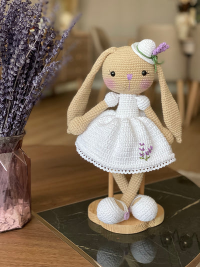 Handmade crocheted Lavender Flower Dressed Bunny Rabbit Toy, complete with a matching hat. This customizable toy includes a name on a leather label and is made using amigurumi techniques. Perfect for nurseries or as a personalized gift.