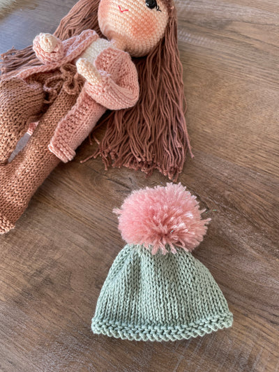 A handcrafted Pink Cardigan Cool Girl Doll with long brown hair, wearing a stylish pink cardigan and beanie, crocheted using the amigurumi technique, and personalized with a custom name on a leather label.