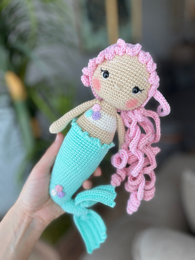 Handmade crochet mermaid doll with pink curly hair and a mint green tail, crafted using the amigurumi technique, personalized with a name on a leather label.