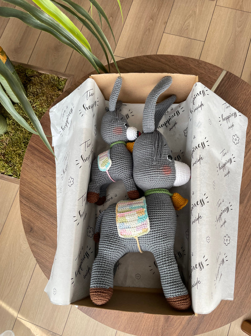 Handmade crochet Donkey Toy set, featuring a pair of amigurumi donkeys with detailed expressions, customized with a name on a leather label. Lying inside a gift box. Perfect gift for kids.