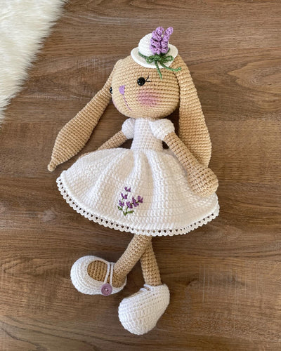 Handmade crocheted Lavender Flower Dressed Bunny Rabbit Toy, complete with a matching hat. This customizable toy includes a name on a leather label and is made using amigurumi techniques. Perfect for nurseries or as a personalized gift.