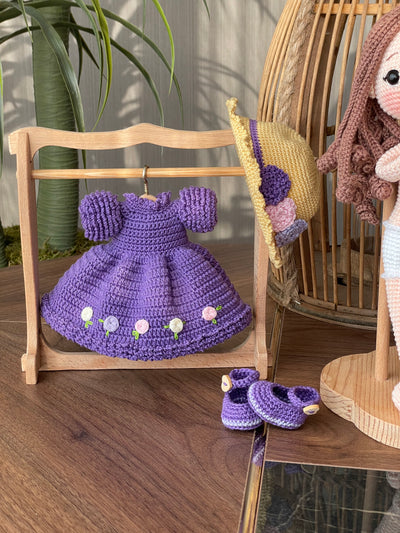 Handmade crocheted Purple Rose Girl Doll with long brown hair, wearing a purple dress with floral accents and a yellow hat. The doll is customizable with a name on a leather label, made using amigurumi techniques. Perfect gift for kids or room decor.