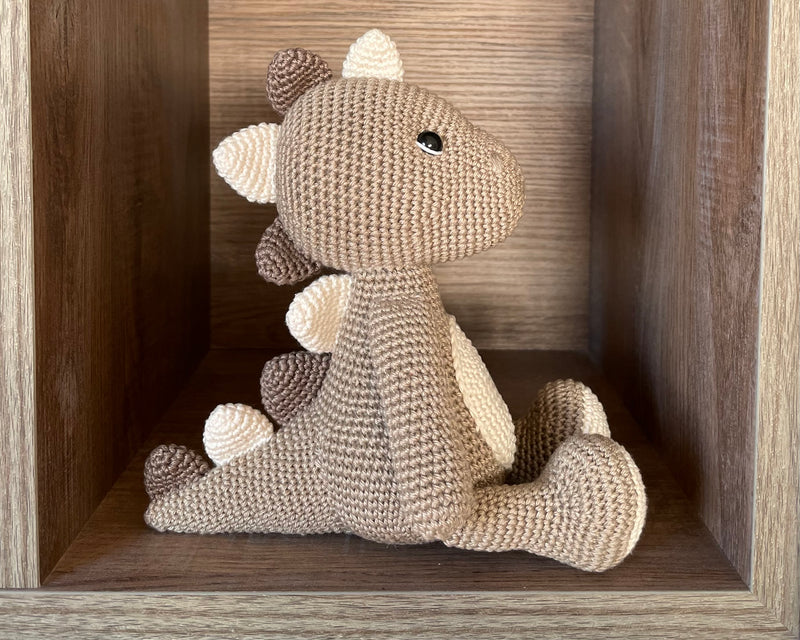 Handmade crochet dinosaur toy in shades of brown and beige, crafted with 100% cotton yarns. This amigurumi dinosaur is customizable with a name on a leather label, perfect for eco-friendly, personalized baby gifts and nursery decor.