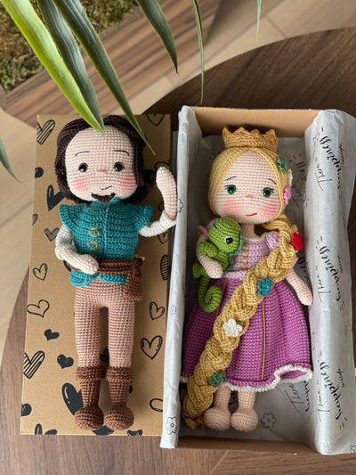 Handmade crocheted Rapunzel and Flynn Rider Dolls with Pascal, featuring intricate details such as Rapunzel's long braided hair and floral accents. Lying inside a gift box. These are customizable with a name on a leather label, perfect as a fairy tale-the