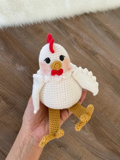 A handmade crocheted Chicken Toy with a cute and detailed design, featuring a red comb and yellow feet. This amigurumi toy is customizable with a name on a leather label, making it a perfect farm-themed nursery decor and personalized gift.