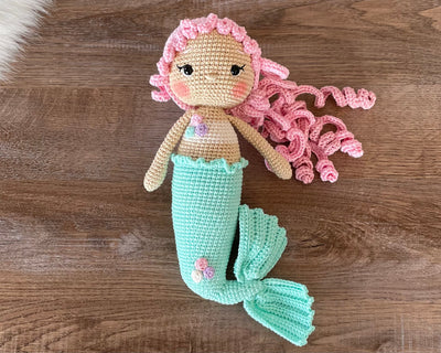 Handmade crochet mermaid doll with pink curly hair and a mint green tail, crafted using the amigurumi technique, personalized with a name on a leather label.