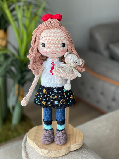 Handmade crochet Idealistic Girl Doll with a red coat, blue scarf, and holding a small teddy bear. This amigurumi doll is customizable with a name on a leather label, perfect for personalized gifts.