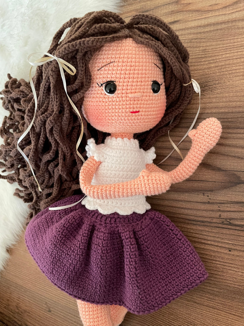 Handmade crocheted Purple Skirted Olivia Doll with long brown hair, a cute skirt, customizable with a name on a leather label. Ideal for nursery decor and as a personalized gift.