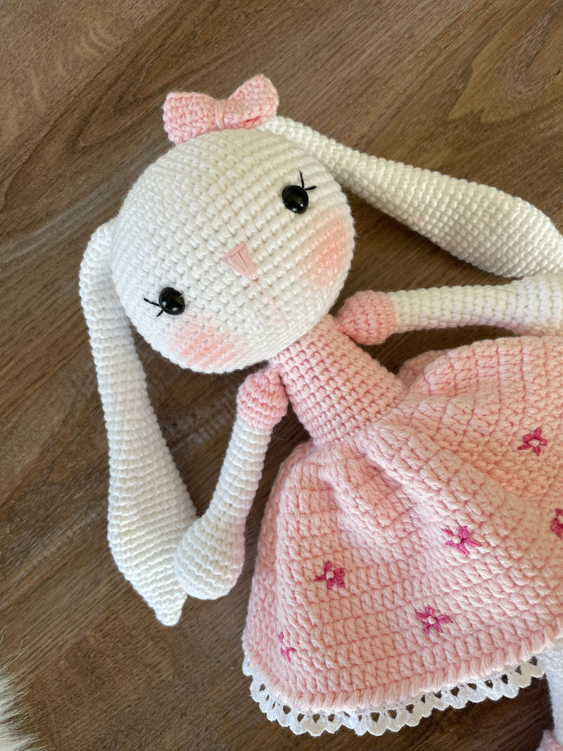 Handmade pink flower bunny rabbit toy crocheted using the amigurumi technique. Features a soft pink dress with floral details and is customizable with a name on a leather label. Perfect baby gift.