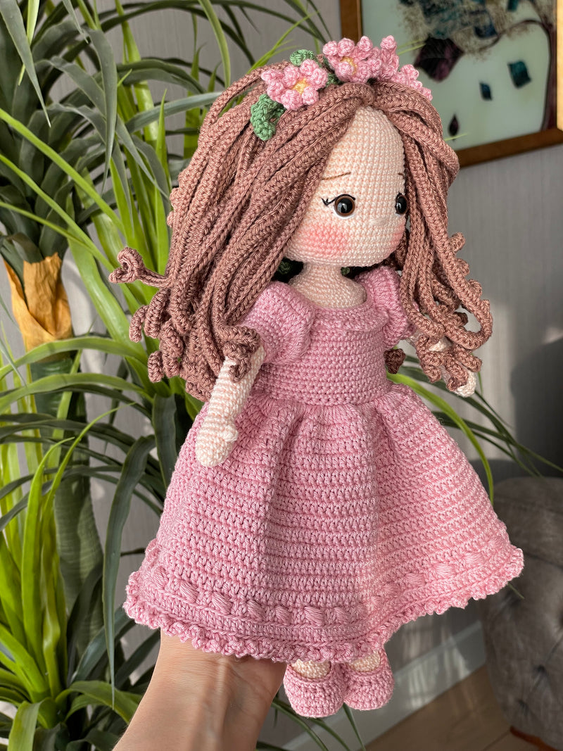 Handmade pink princess girl doll, crocheted using amigurumi technique. Features a beautiful dress and flower crown, customizable with a name on a leather label. Perfect for kids and collectors.