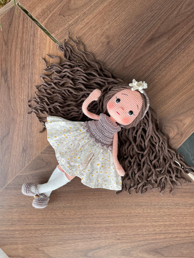 Handmade crocheted Daisy Dressed Olivia Doll with long brown hair and a floral dress, customizable with a name on a leather label. Perfect for nursery decor and as a personalized gift.