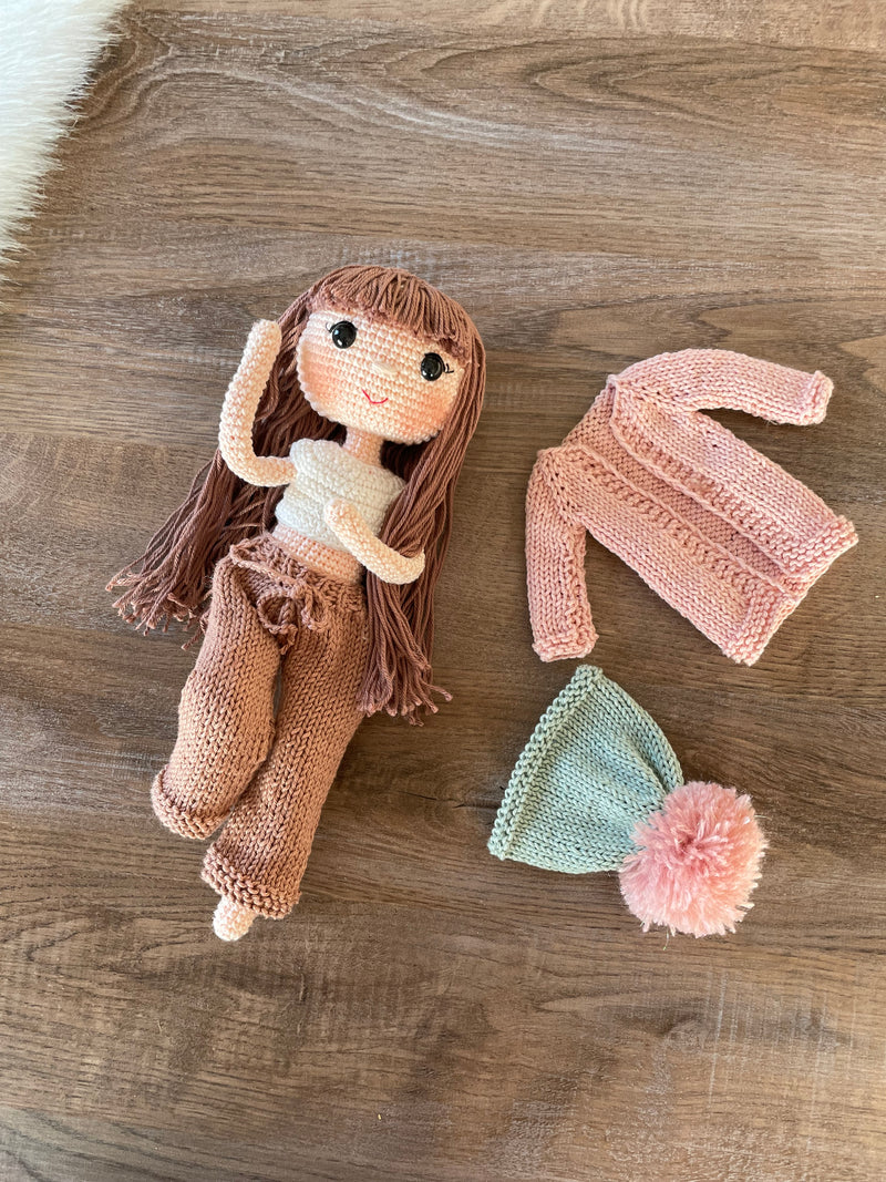 A handcrafted Pink Cardigan Cool Girl Doll with long brown hair, wearing a stylish pink cardigan and beanie, crocheted using the amigurumi technique, and personalized with a custom name on a leather label.