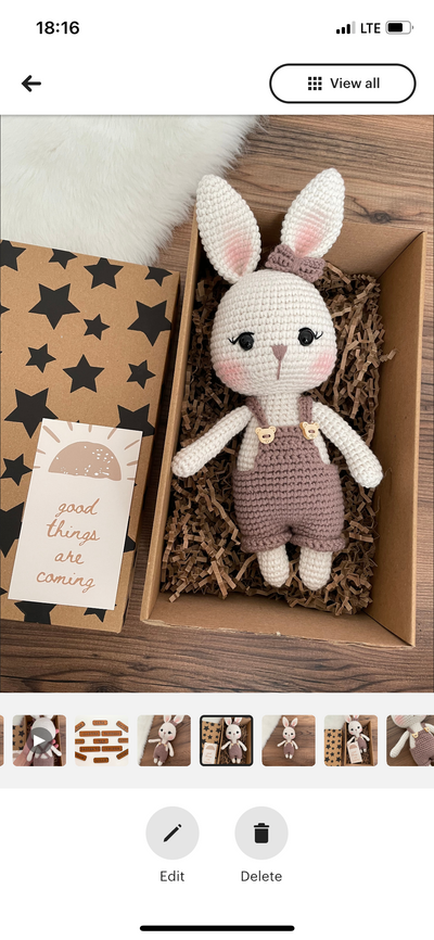 A mink color handmade crocheted Overall Girl Bunny Rabbit Toy with a cute bow and overalls, lying inside a gift box. This amigurumi bunny doll is customizable with a name on a leather label, making it an ideal choice for nursery decor and personalized gif