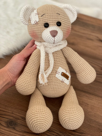 A handmade beige teddy bear toy crafted with the amigurumi technique, featuring a soft texture, a personalized leather name patch, and a cute, cuddly design.