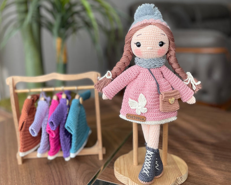 Handmade Pink Winter Girl Doll in a pink coat, gray scarf, and hat with braids, made with 100% cotton yarn, customizable with a name on a leather label, perfect for unique baby gifts and imaginative play.