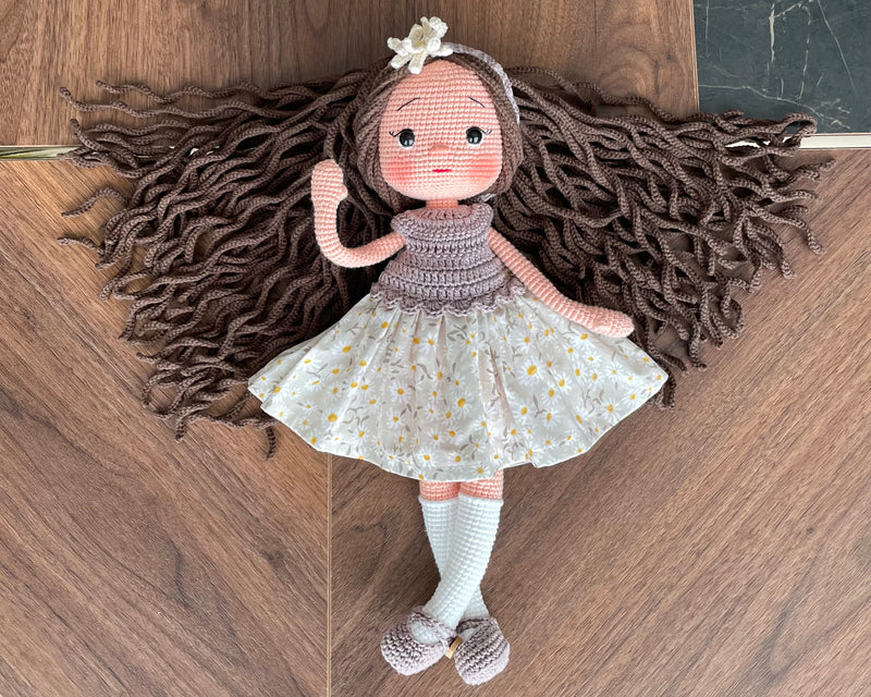 Handmade crocheted Daisy Dressed Olivia Doll with long brown hair and a floral dress, customizable with a name on a leather label. Perfect for nursery decor and as a personalized gift.