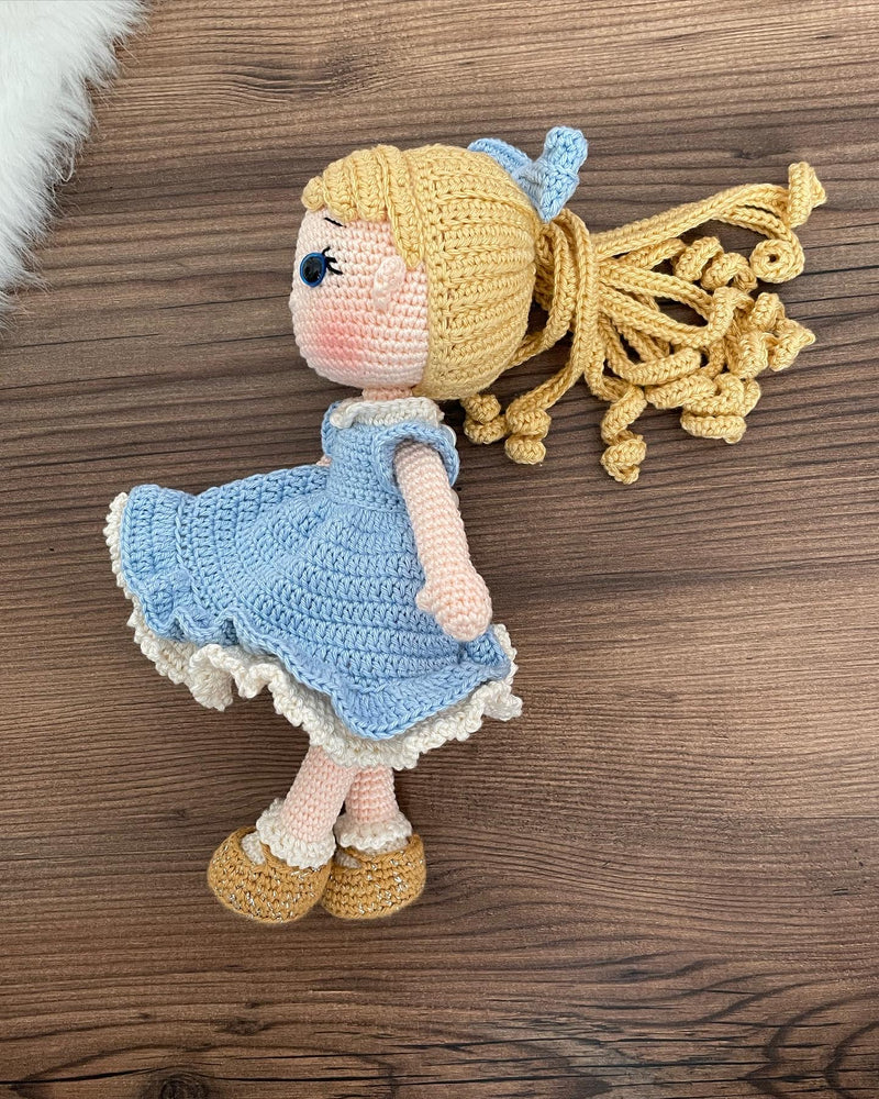 Handmade Blue Nina Doll with blonde hair, wearing a blue dress and a matching bow, made with 100% cotton yarn, customizable with a name on a leather label.