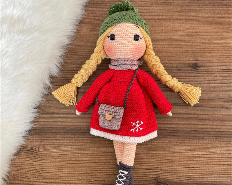 Handmade crocheted Red Snowflake Girl Doll featuring a red dress, snowflake detail, and a cute braided hairstyle. Customizable with a name on a leather label, made using amigurumi techniques. Perfect as a personalized gift or nursery decor.