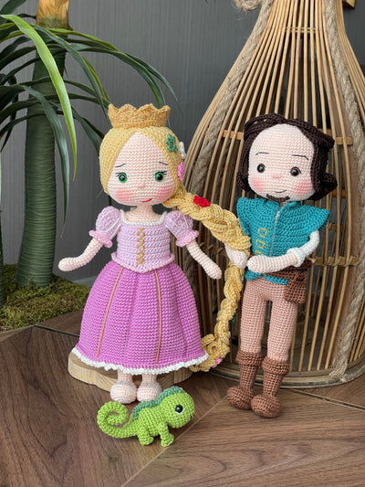 Handmade crocheted Rapunzel and Flynn Rider Dolls with Pascal, featuring intricate details such as Rapunzel's long braided hair and floral accents. These are customizable with a name on a leather label, perfect as a fairy tale-themed gift or decor.