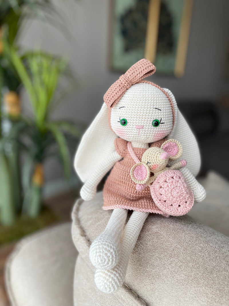 Handmade crocheted amigurumi bunny rabbit doll with a small mouse toy, dressed in pink, made of 100% cotton, customizable with a name on a leather label, perfect for nursery decor.