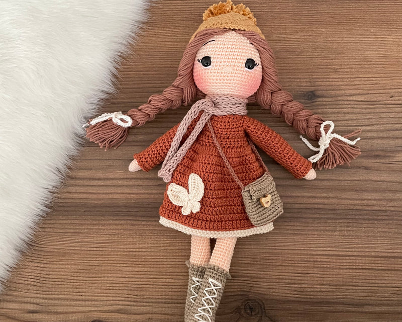 Handmade crochet winter girl doll in a brick-colored dress and beige hat, mink scarf, crafted with 100% cotton yarns, personalized with a custom name on a leather label, perfect for unique girl gifts and imaginative play.