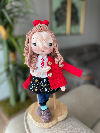 Handmade crochet Idealistic Girl Doll with a red coat, blue scarf, and holding a small teddy bear. This amigurumi doll is customizable with a name on a leather label, perfect for personalized gifts.