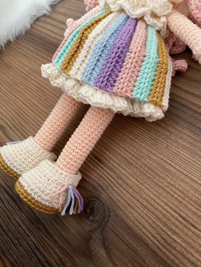 A handmade crocheted Unicorn Girl Doll with pastel rainbow dress, pink curly hair, and a golden horn. This amigurumi toy is customizable with a name on a leather label, perfect for nursery decor and personalized gifts.