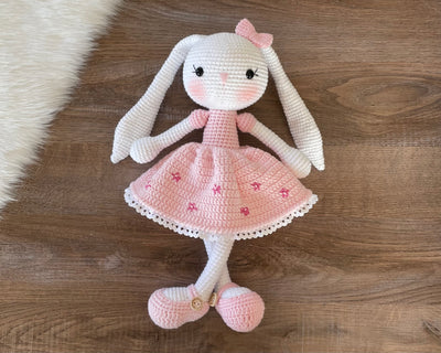 Handmade pink flower bunny rabbit toy crocheted using the amigurumi technique. Features a soft pink dress with floral details and is customizable with a name on a leather label. Perfect baby gift.