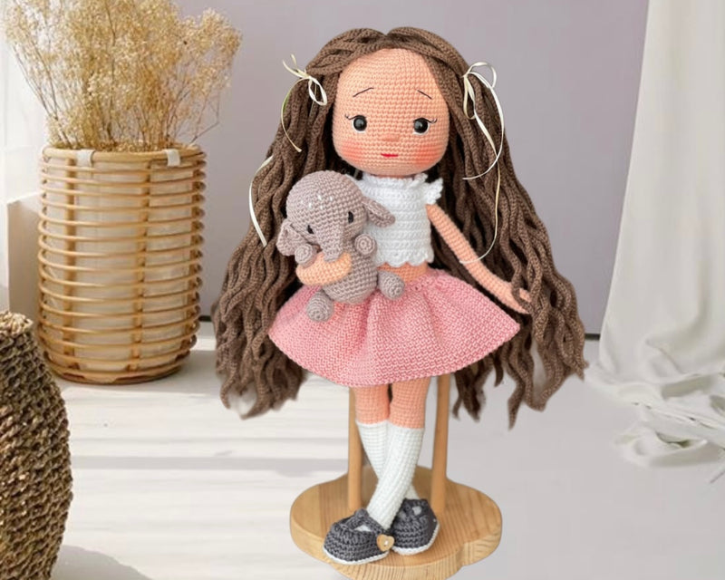 Handmade crocheted Pink Skirted Olivia Doll with long brown hair, a cute skirt, and a tiny elephant, customizable with a name on a leather label. Ideal for nursery decor and as a personalized gift.