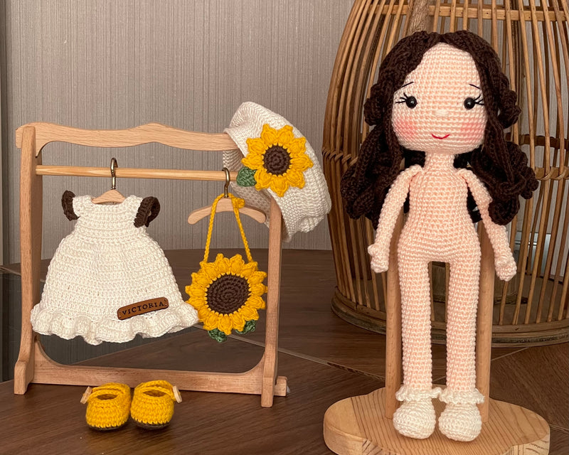 A handmade Sunflower Girl Doll with dark brown hair, wearing a white dress adorned with sunflowers, a matching sunflower beret, and yellow shoes, crocheted using the amigurumi technique and personalized with a custom name on a leather label.