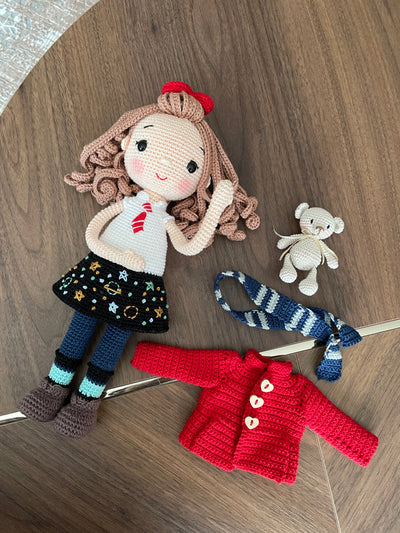 Handmade crochet Idealistic Girl Doll with a red coat, blue scarf, and holding a small teddy bear. This amigurumi doll is customizable with a name on a leather label, perfect for personalized gifts.