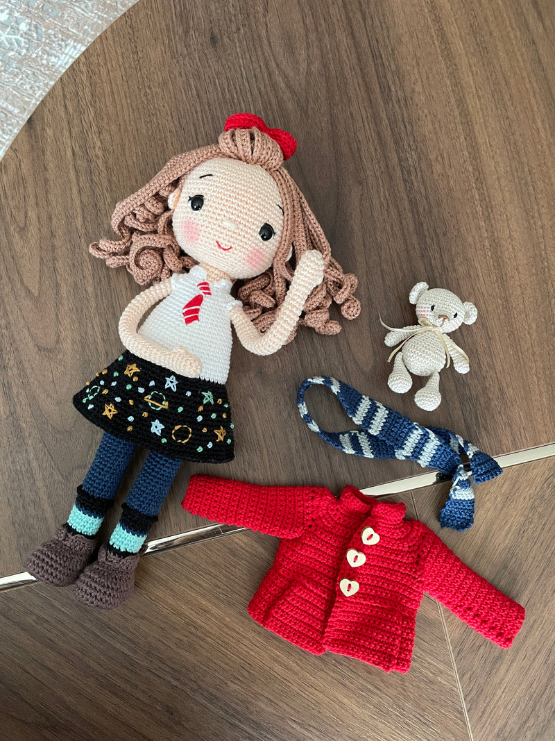 Handmade crochet Idealistic Girl Doll with a red coat, blue scarf, and holding a small teddy bear. This amigurumi doll is customizable with a name on a leather label, perfect for personalized gifts.