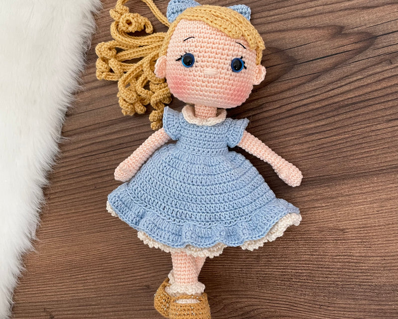 Handmade Blue Nina Doll with blonde hair, wearing a blue dress and a matching bow, made with 100% cotton yarn, customizable with a name on a leather label, perfect for unique girl gifts and imaginative play.