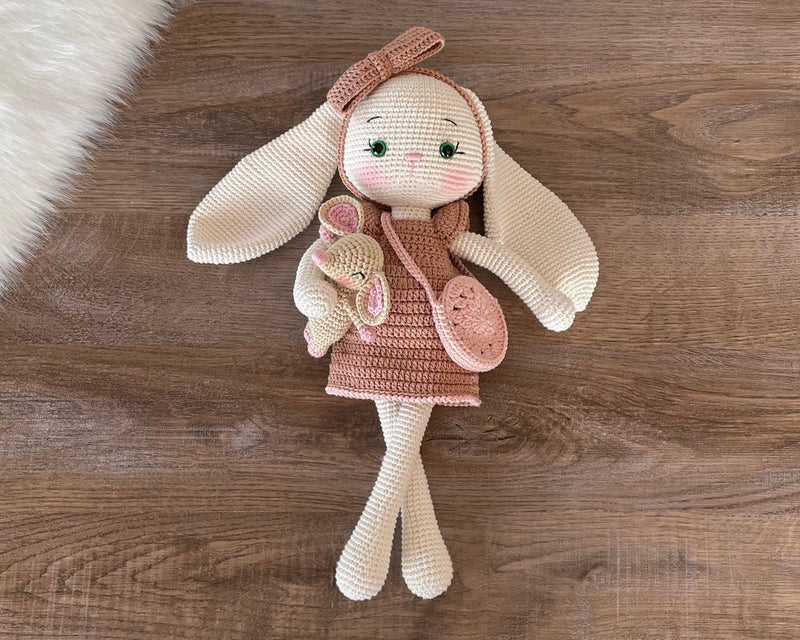 Handmade crocheted amigurumi bunny rabbit doll with a small mouse toy, dressed in pink, made of 100% cotton, customizable with a name on a leather label, perfect for nursery decor.