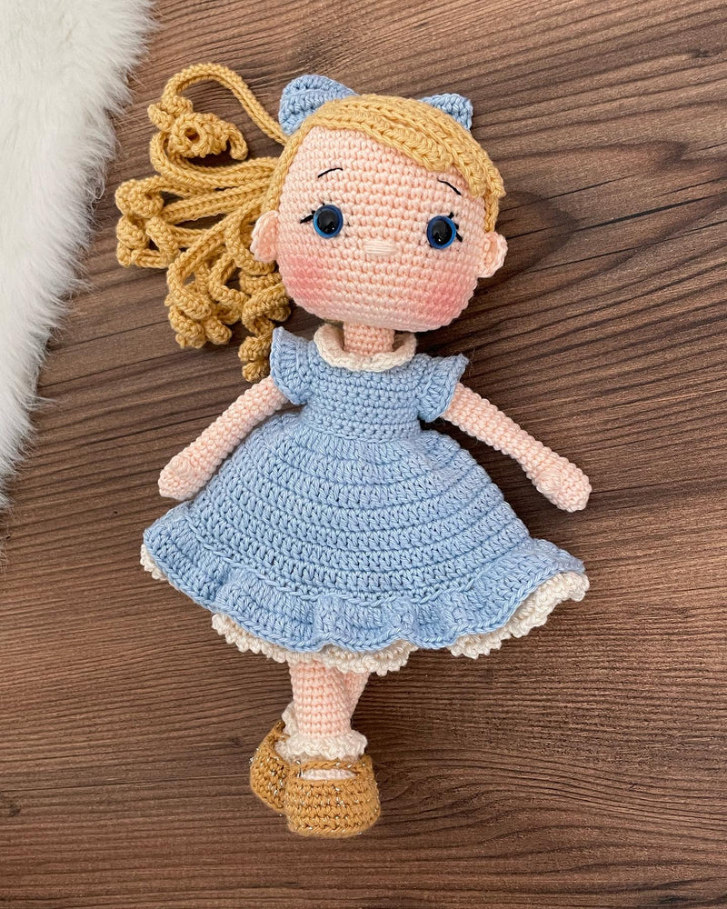 Handmade Blue Nina Doll with blonde hair, wearing a blue dress and a matching bow, made with 100% cotton yarn, customizable with a name on a leather label.