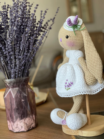 Handmade crocheted Lavender Flower Dressed Bunny Rabbit Toy, complete with a matching hat. This customizable toy includes a name on a leather label and is made using amigurumi techniques. Perfect for nurseries or as a personalized gift.