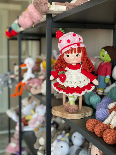 Handmade strawberry shortcake crochet doll with red hair, wearing a strawberry-themed outfit. Features a pink hat with red polka dots, red dress with white apron, and striped stockings. Perfect for children and collectors.