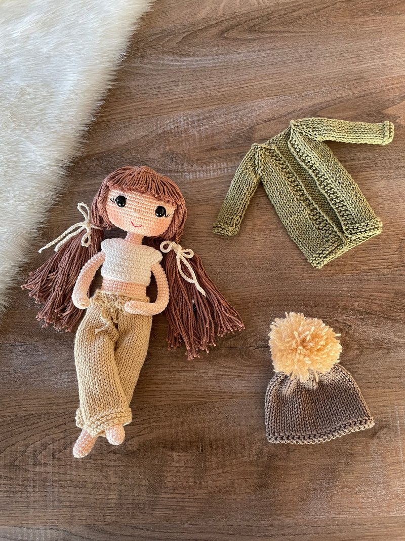 A handcrafted Green Cardigan Cool Girl Doll with long brown hair, wearing a stylish green cardigan and beanie, crocheted using the amigurumi technique, and personalized with a custom name on a leather label.