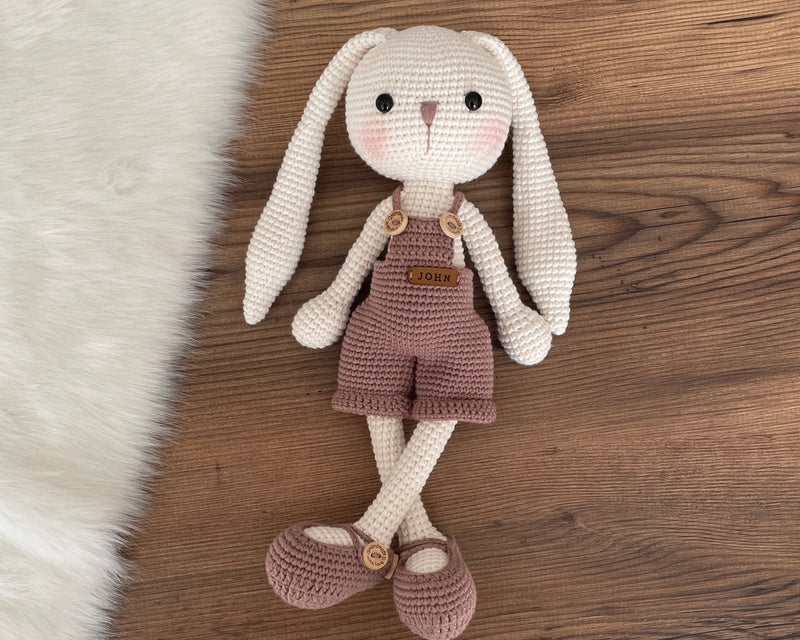 Handmade mink color overall bunny rabbit toy, crocheted using amigurumi technique with long ears and a custom name on a leather label, perfect for gifts.