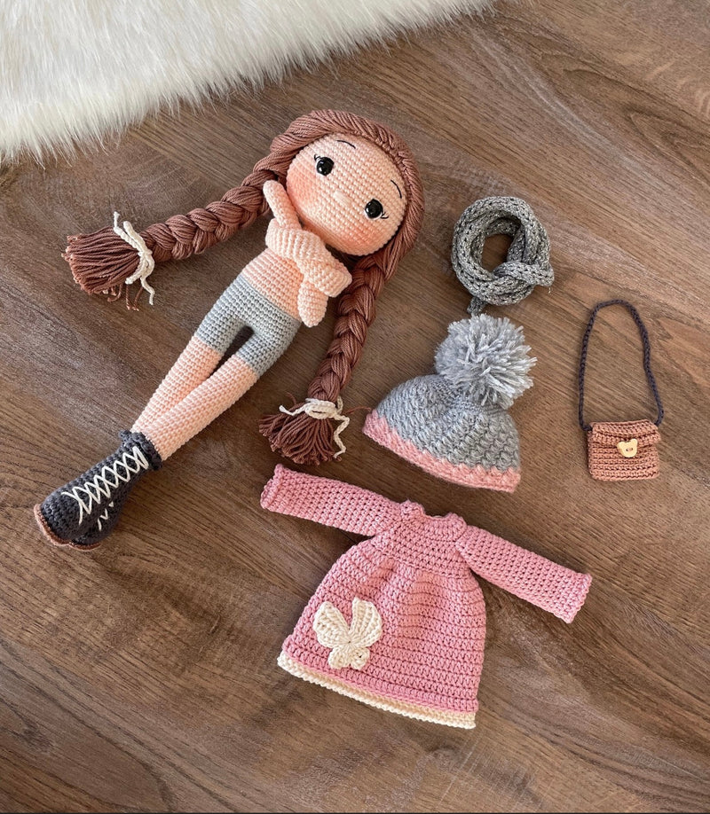 Handmade Pink Winter Girl Doll in a pink coat, gray scarf, and hat with braids, made with 100% cotton yarn, customizable with a name on a leather label.