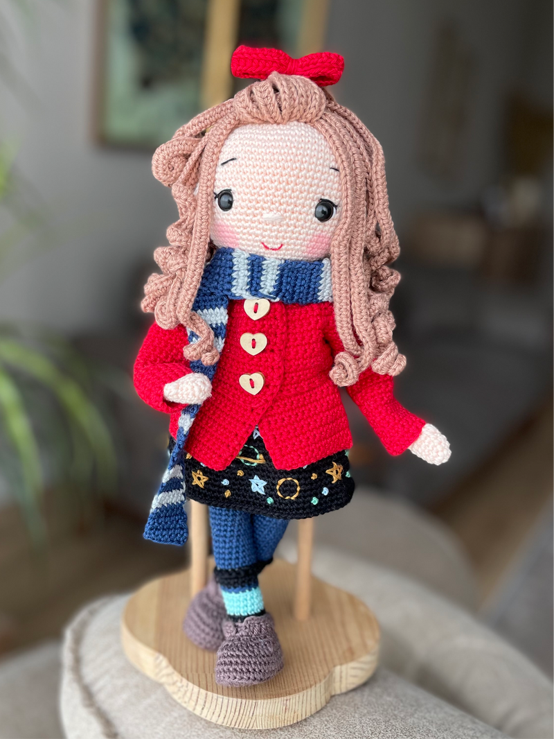 Handmade crochet Idealistic Girl Doll with a red coat, blue scarf, and holding a small teddy bear. This amigurumi doll is customizable with a name on a leather label, perfect for personalized gifts.