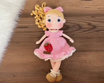 Handmade Pink Nina Doll with blonde hair, wearing a pink dress with a strawberry detail, made with 100% cotton yarn, customizable with a name on a leather label, perfect for unique girl gifts and imaginative play.