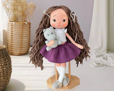 Handmade crocheted Purple Skirted Olivia Doll with long brown hair, a cute skirt, and a tiny hippo, customizable with a name on a leather label. Ideal for nursery decor and as a personalized gift.