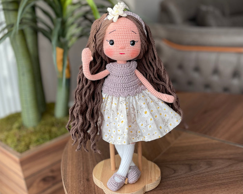 Handmade crocheted Daisy Dressed Olivia Doll with long brown hair and a floral dress, customizable with a name on a leather label. Perfect for nursery decor and as a personalized gift.