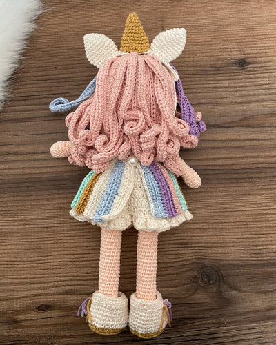 A handmade crocheted Unicorn Girl Doll with pastel rainbow dress, pink curly hair, and a golden horn. This amigurumi toy is customizable with a name on a leather label, perfect for nursery decor and personalized gifts.