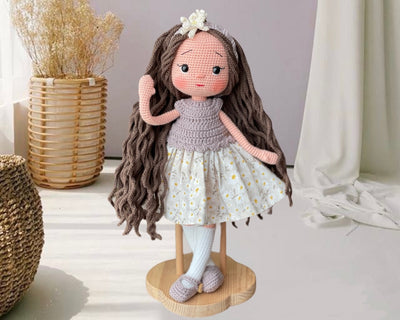 Handmade crocheted Daisy Dressed Olivia Doll with long brown hair and a floral dress, customizable with a name on a leather label. Perfect for nursery decor and as a personalized gift.